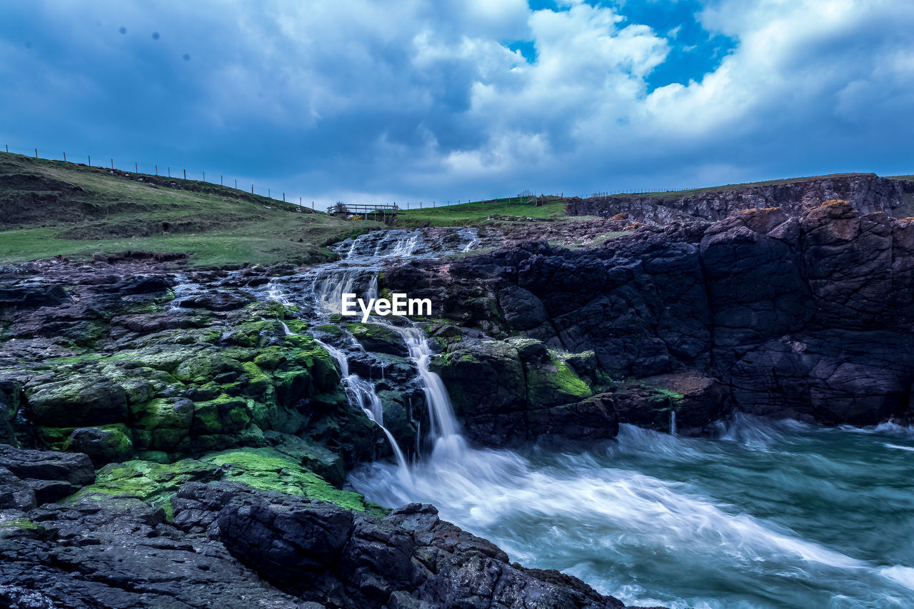 SCENIC VIEW OF WATERFALL AGAINST ROCKS