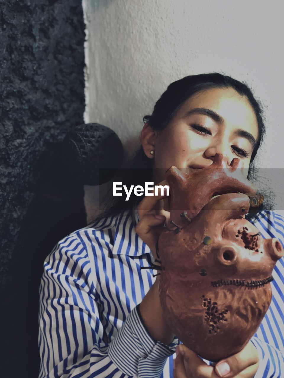 Young woman looking while holding heart model against wall