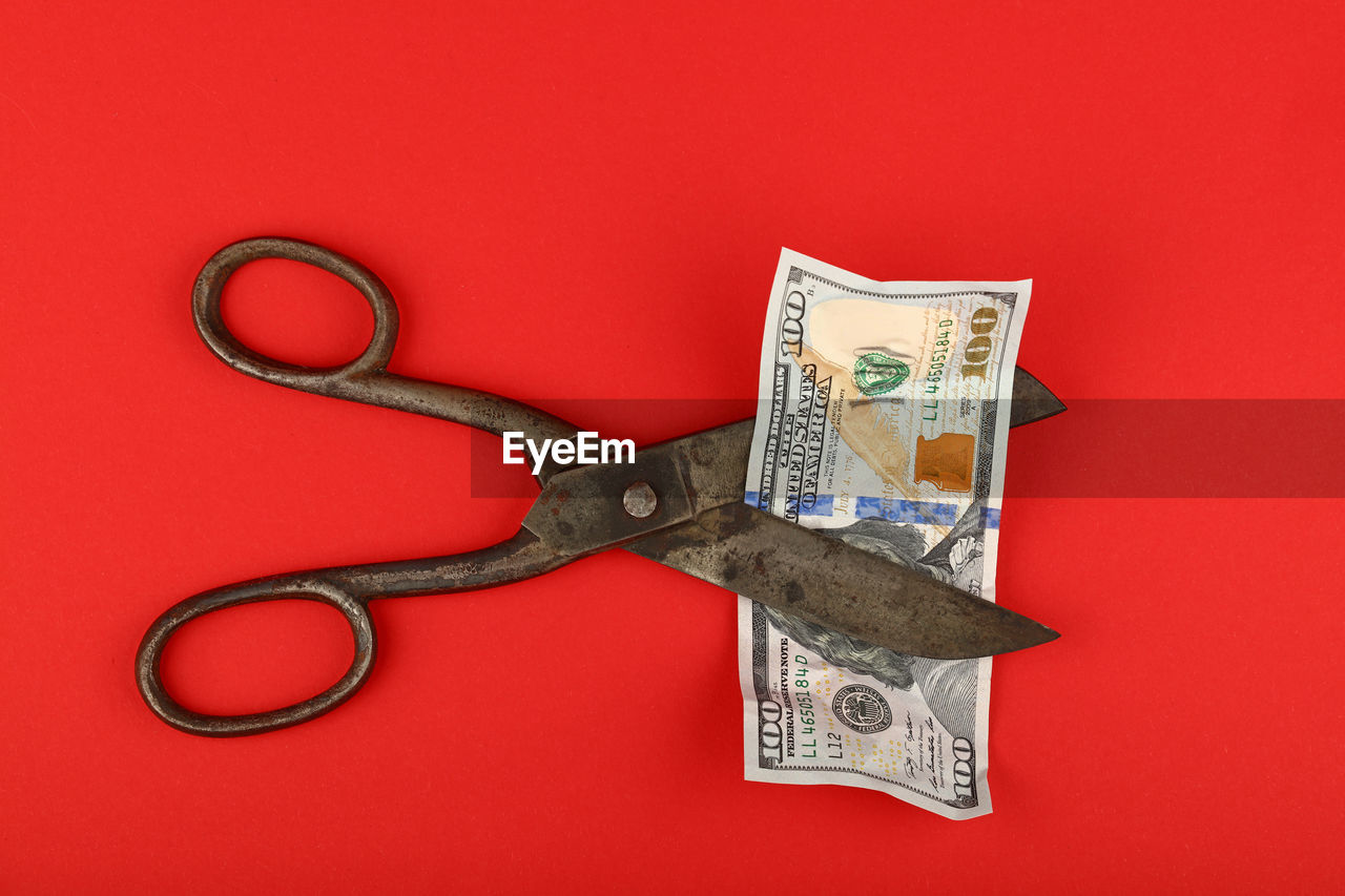 Directly above shot of scissors cutting american one hundred dollar bill on red background