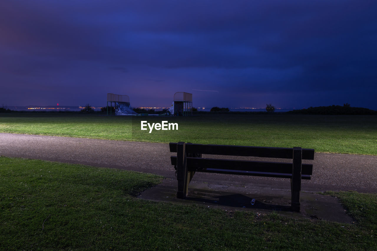 EMPTY BENCHES ON FIELD AGAINST SKY