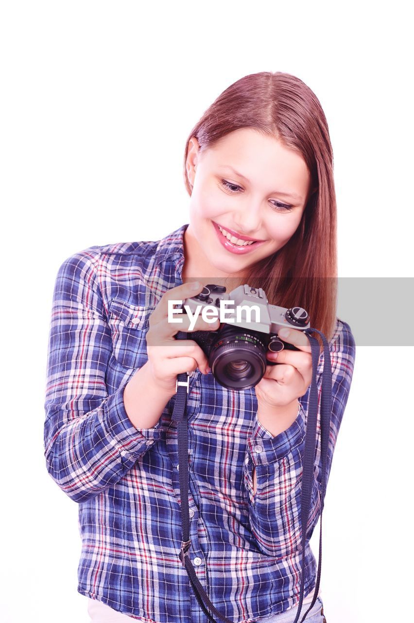 Smiling young woman holding camera against white background