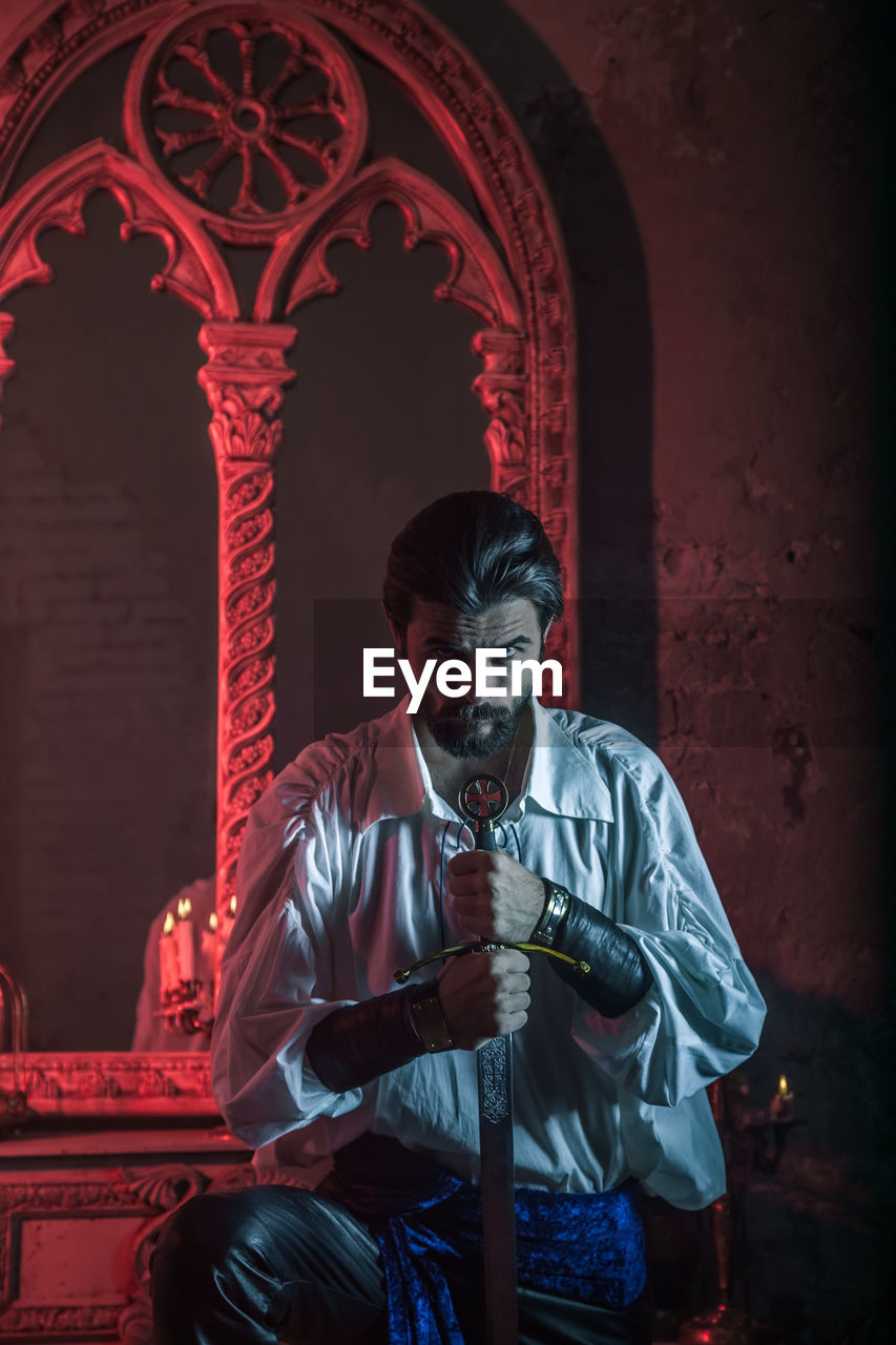 Portrait of man in costume holding sword at abandoned building during night