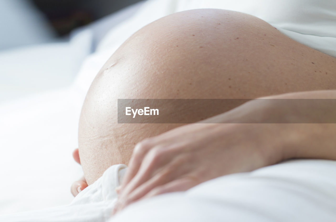 Close-up midsection of pregnant woman lying on bed