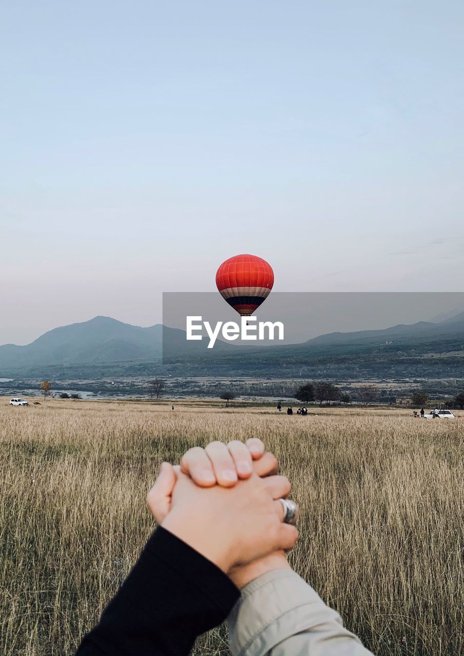 Cropped image of couple holding hands against hot air balloon over landscape