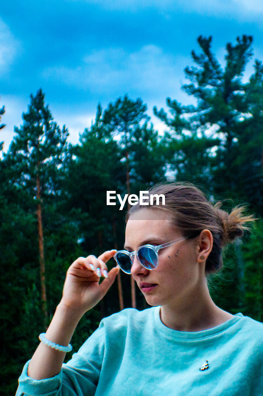 PORTRAIT OF WOMAN HOLDING SUNGLASSES AGAINST TREE