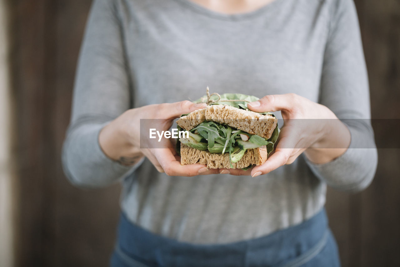 Midsection of woman holding sandwich while standing at home