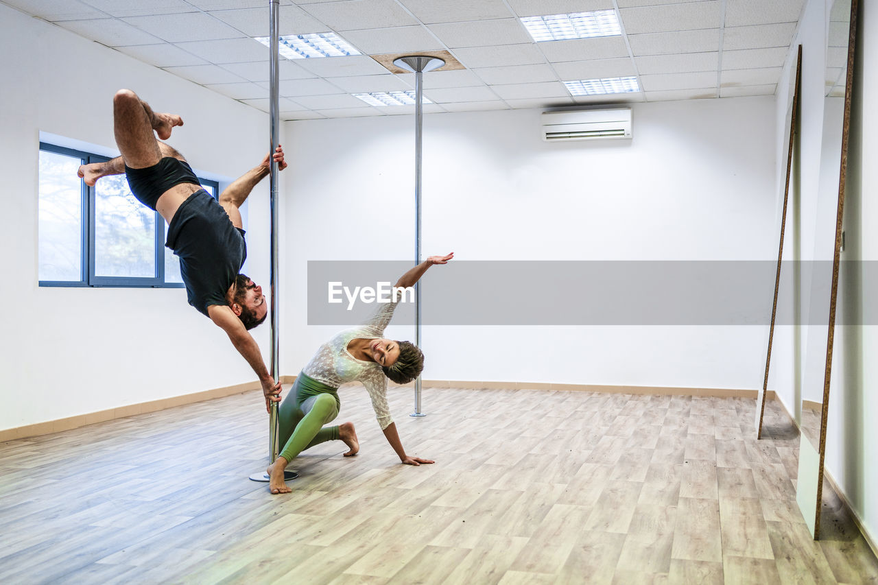 Mid adult male acrobat balancing on rod by woman in dance studio