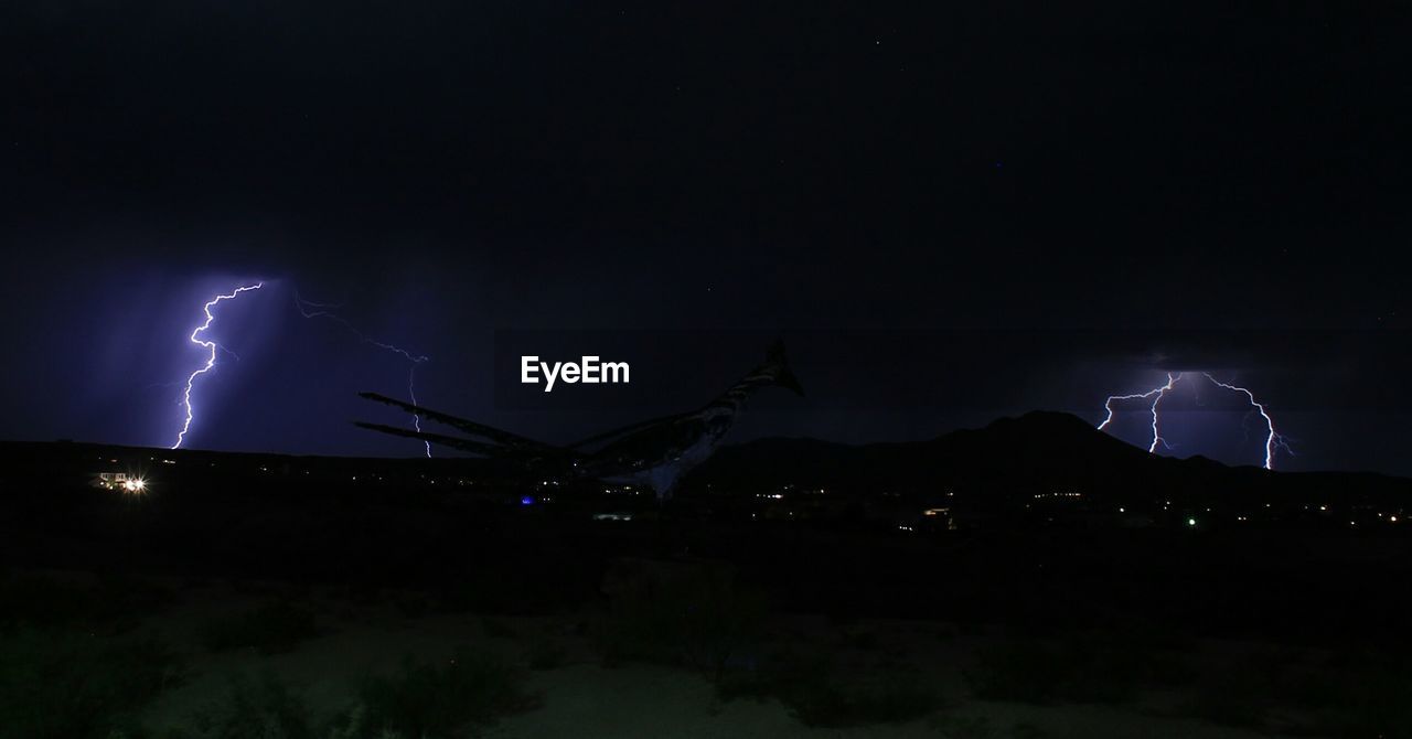 LIGHTNING OVER ILLUMINATED MOUNTAINS AGAINST SKY