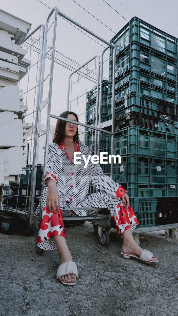 FULL LENGTH OF WOMAN SITTING AGAINST BUILDINGS