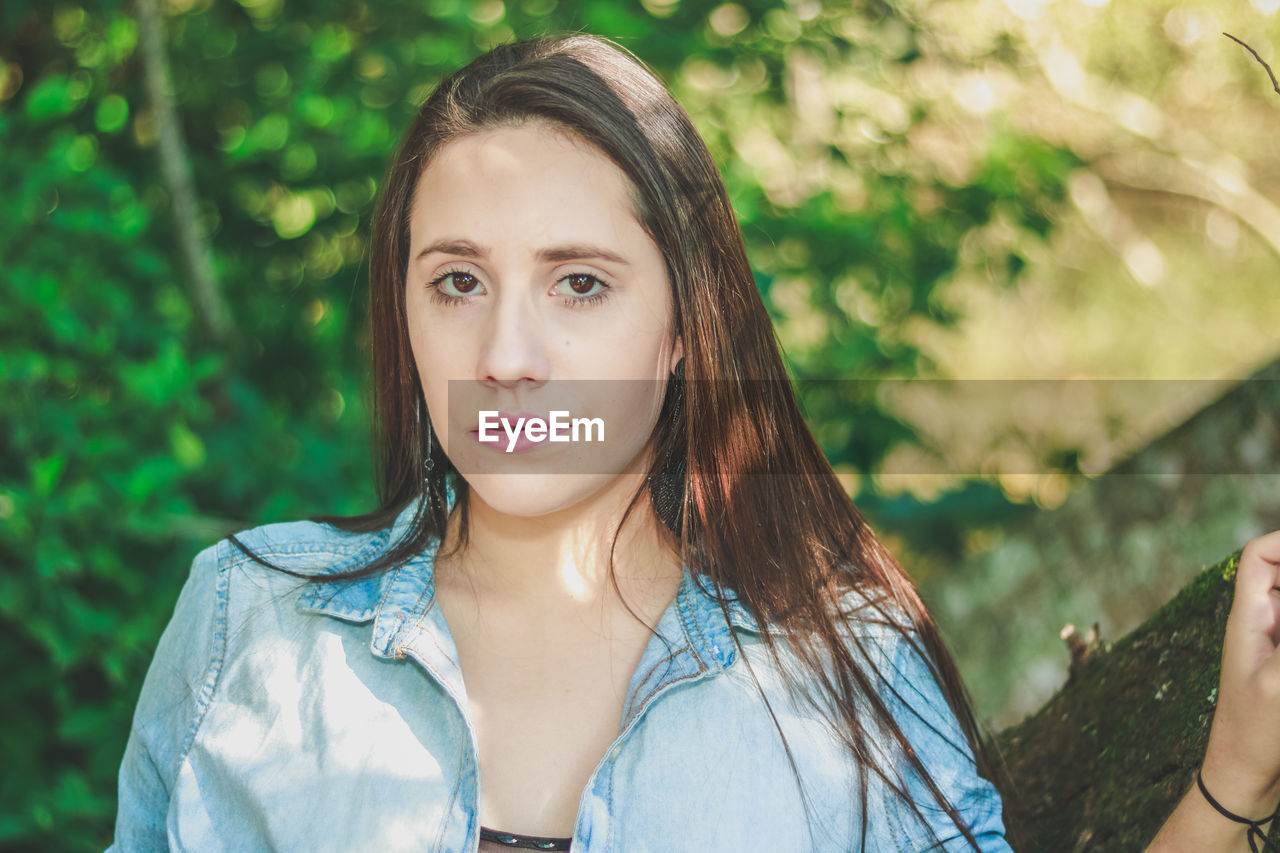 Close-up portrait of young woman against trees