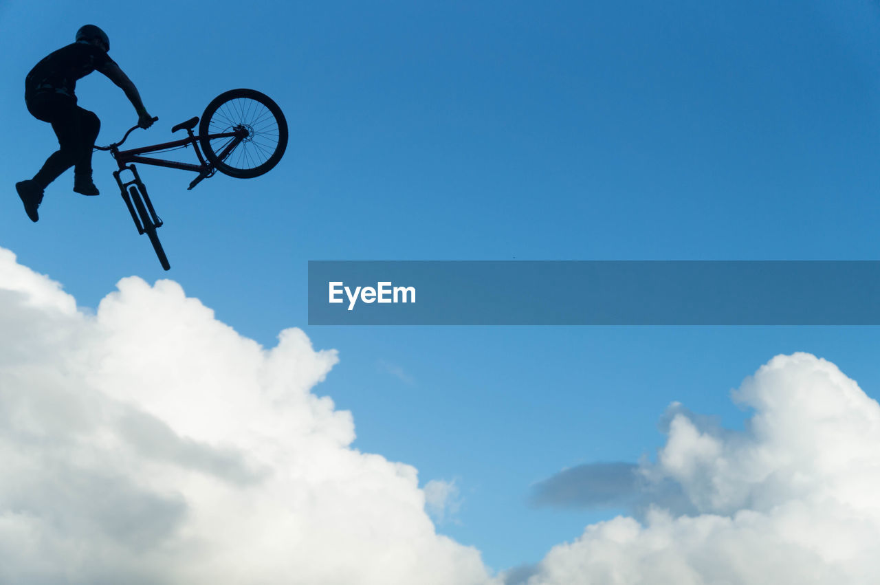 Low angle view of silhouette man doing stunt with bicycle against blue sky