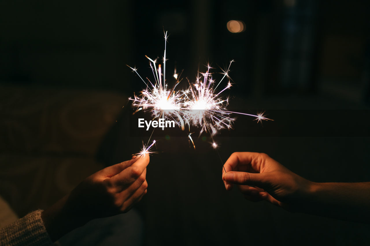 Cropped image of hands holding sparklers at night