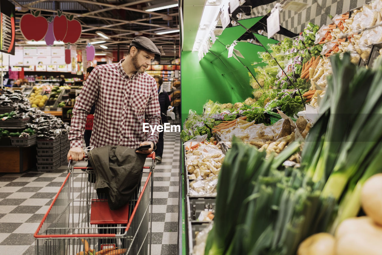 Man holding smart phone while choosing vegetables in supermarket