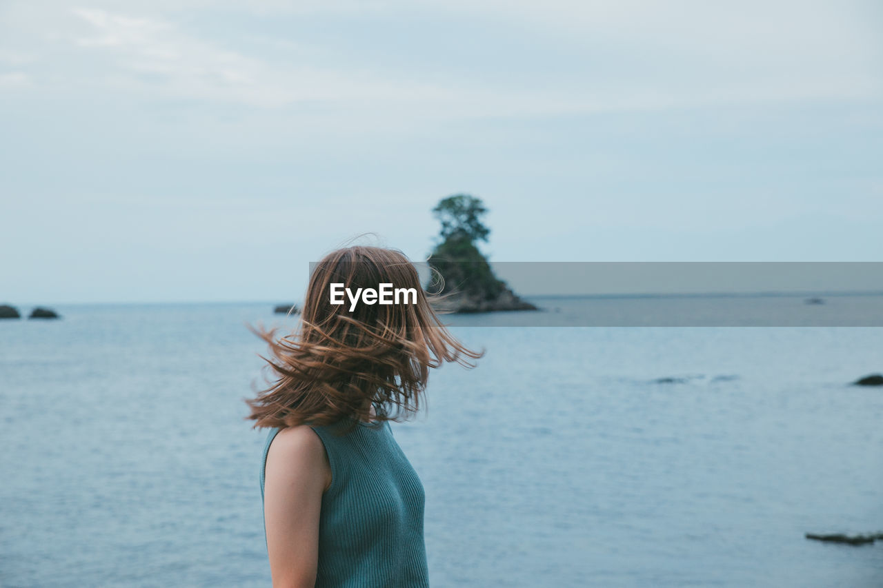 Woman tossing hair standing by sea against sky