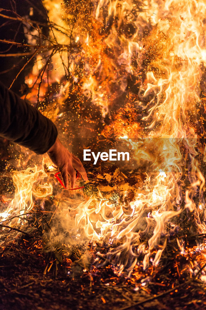 Cropped hand throwing firewood in fire at night