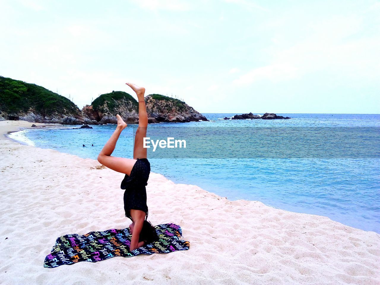 Side view of woman practicing headstand at beach