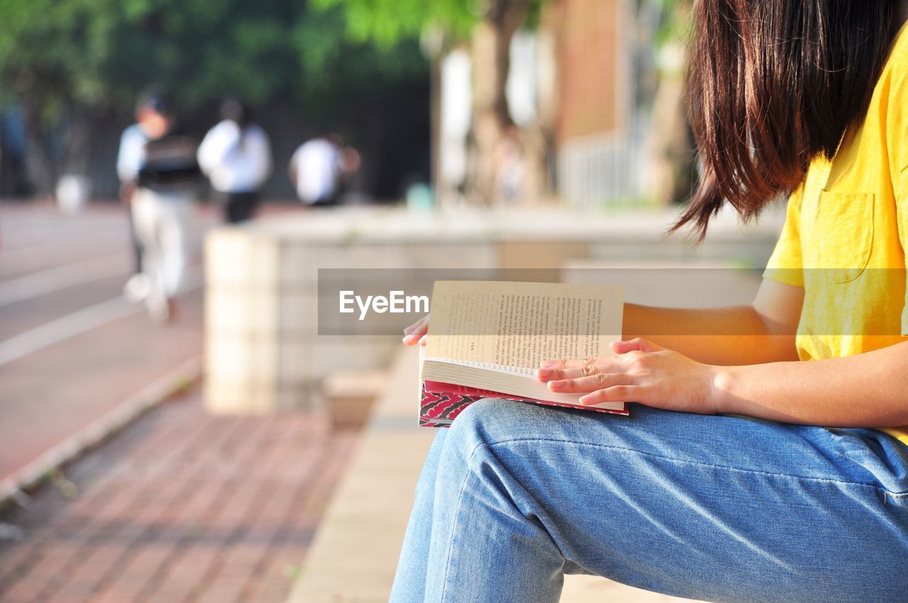 Midsection of woman reading book while sitting on bench