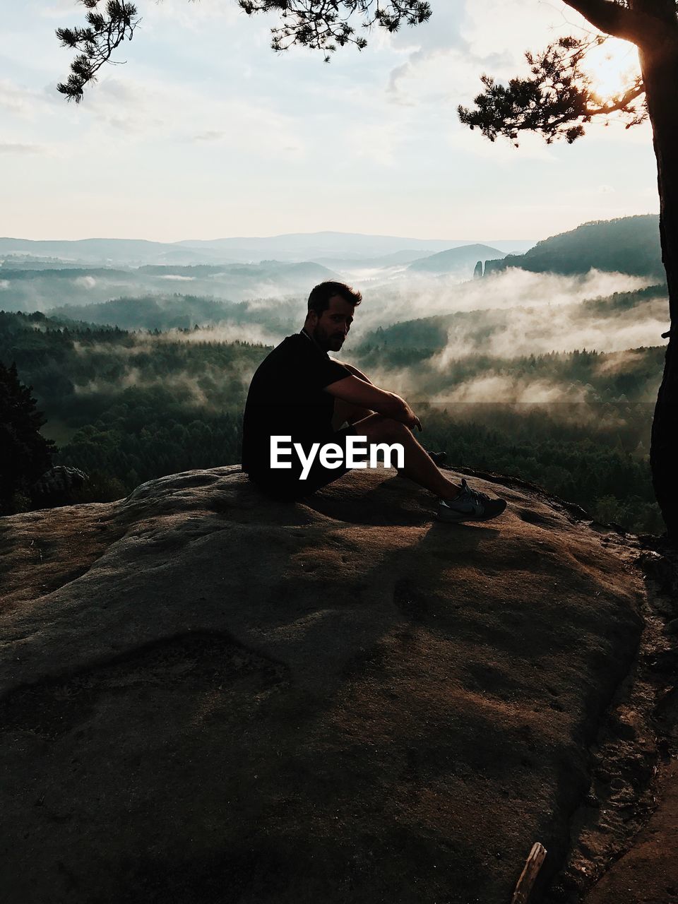 MAN SITTING ON LANDSCAPE AGAINST MOUNTAIN RANGE