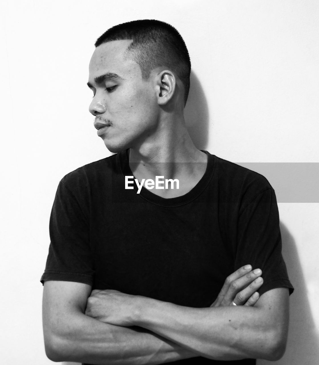 black, one person, black and white, studio shot, waist up, indoors, adult, monochrome photography, arms crossed, white, portrait, monochrome, casual clothing, men, t-shirt, arm, person, young adult, shaved head, sitting, looking, lifestyles, white background, front view, hand, looking away, contemplation, clothing, emotion, hairstyle, standing