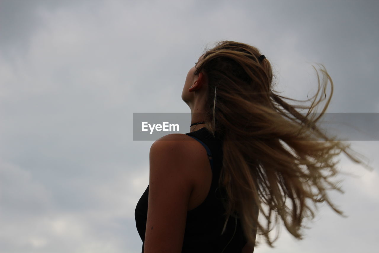 Low angle view of woman with tousled hair looking at sky