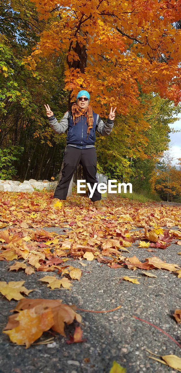 MAN STANDING BY AUTUMN LEAVES