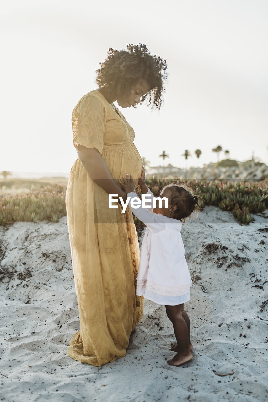 Full length view of young toddler girl with mother’s pregnant belly