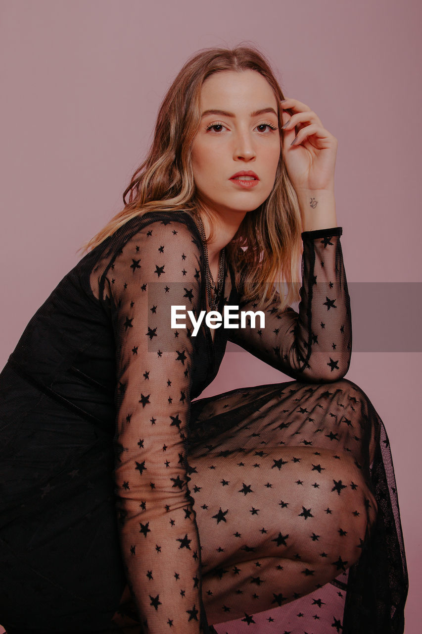 Portrait of young woman sitting against pink background