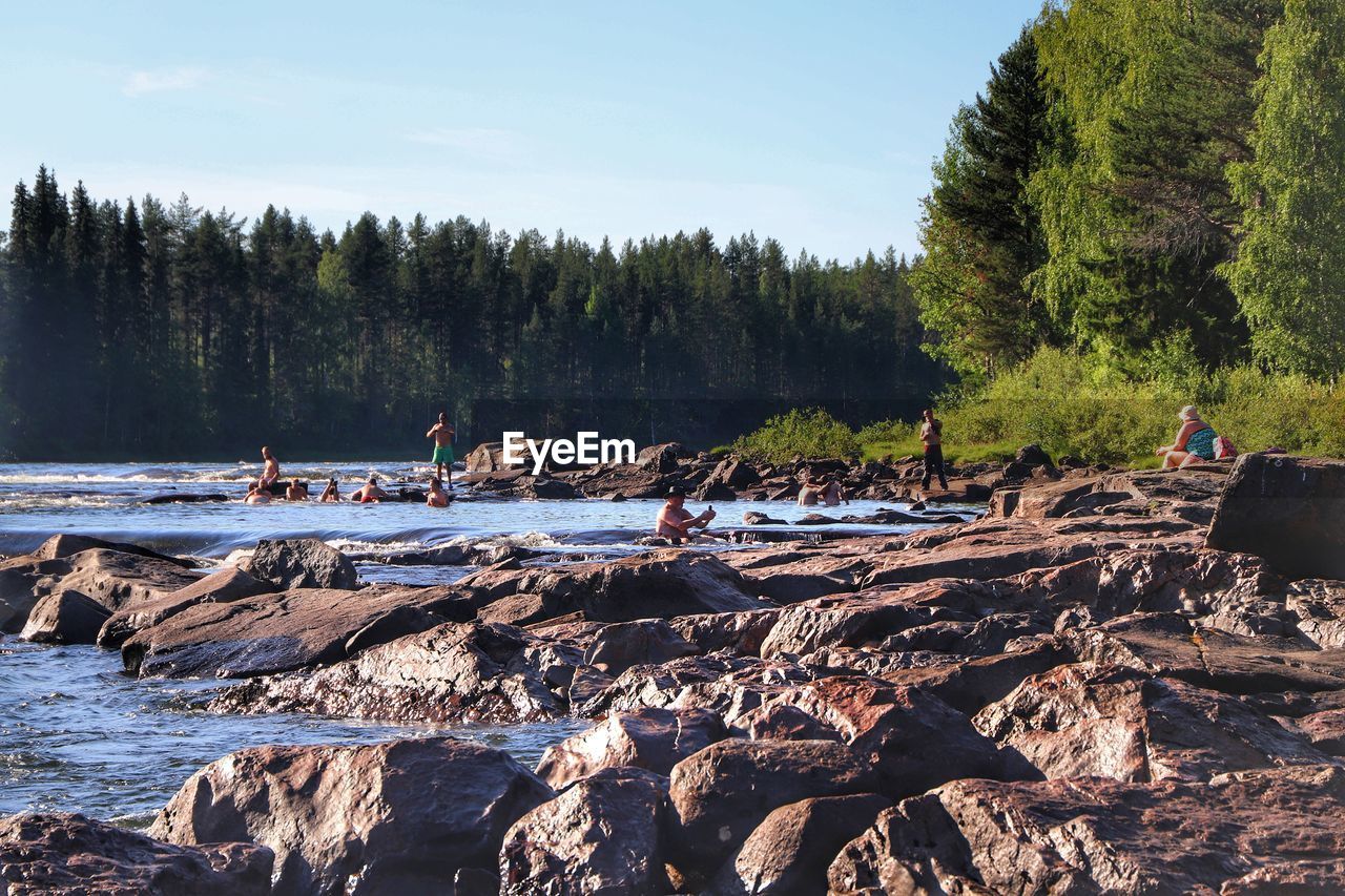 GROUP OF PEOPLE ON ROCKS BY THE SHORE