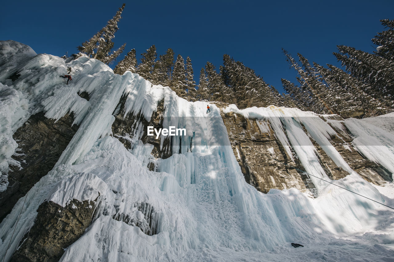 Low angle view of woman climbing on snowcapped mountain during winter