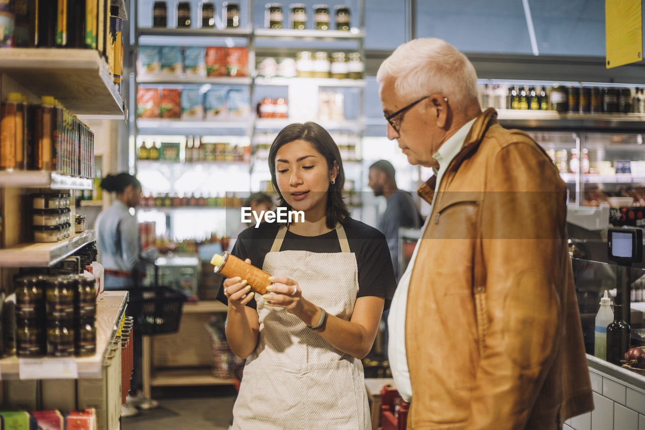 Saleswoman discussing over product with senior male customer at delicatessen