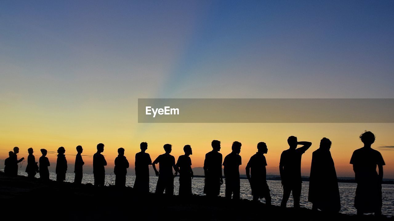 Silhouette people standing by sea against sky during sunset