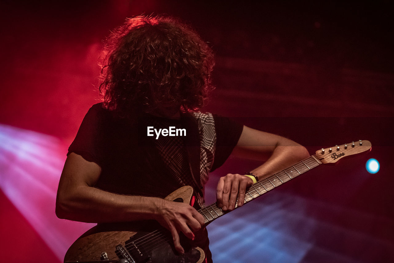 MAN PLAYING GUITAR AT ILLUMINATED STAGE