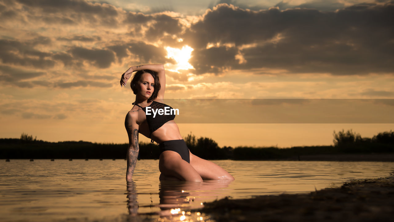 Young woman in lake against sky during sunset