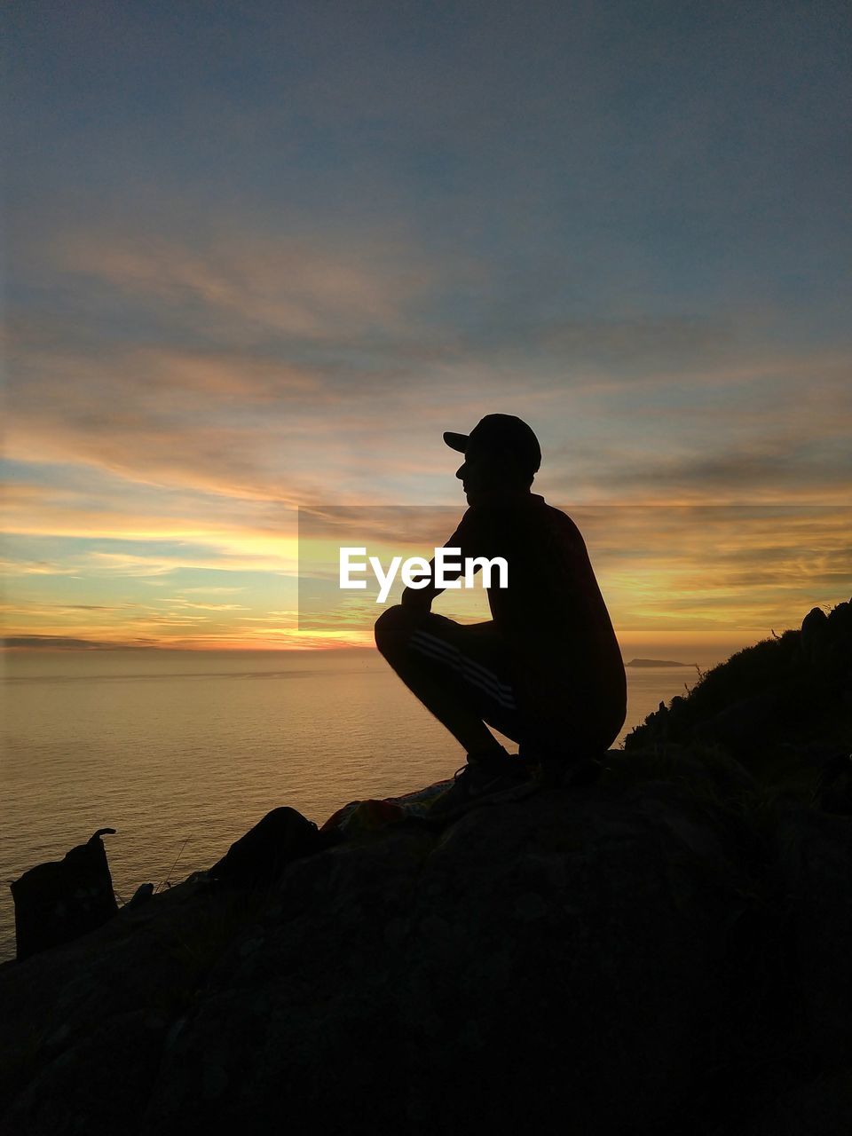 Silhouette man sitting on rock against sea during sunset