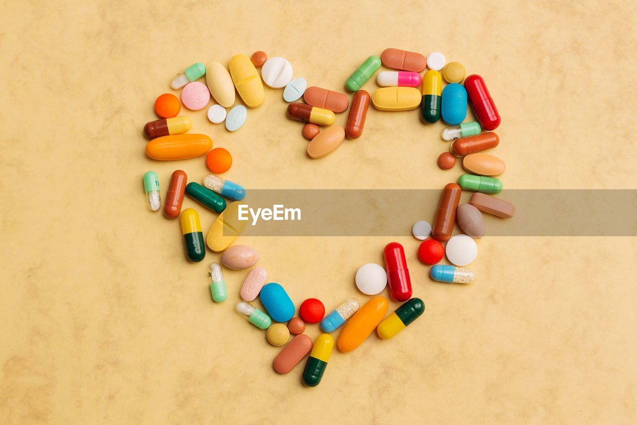 Directly above shot of multi colored medicines arranged in heart shape on beige background