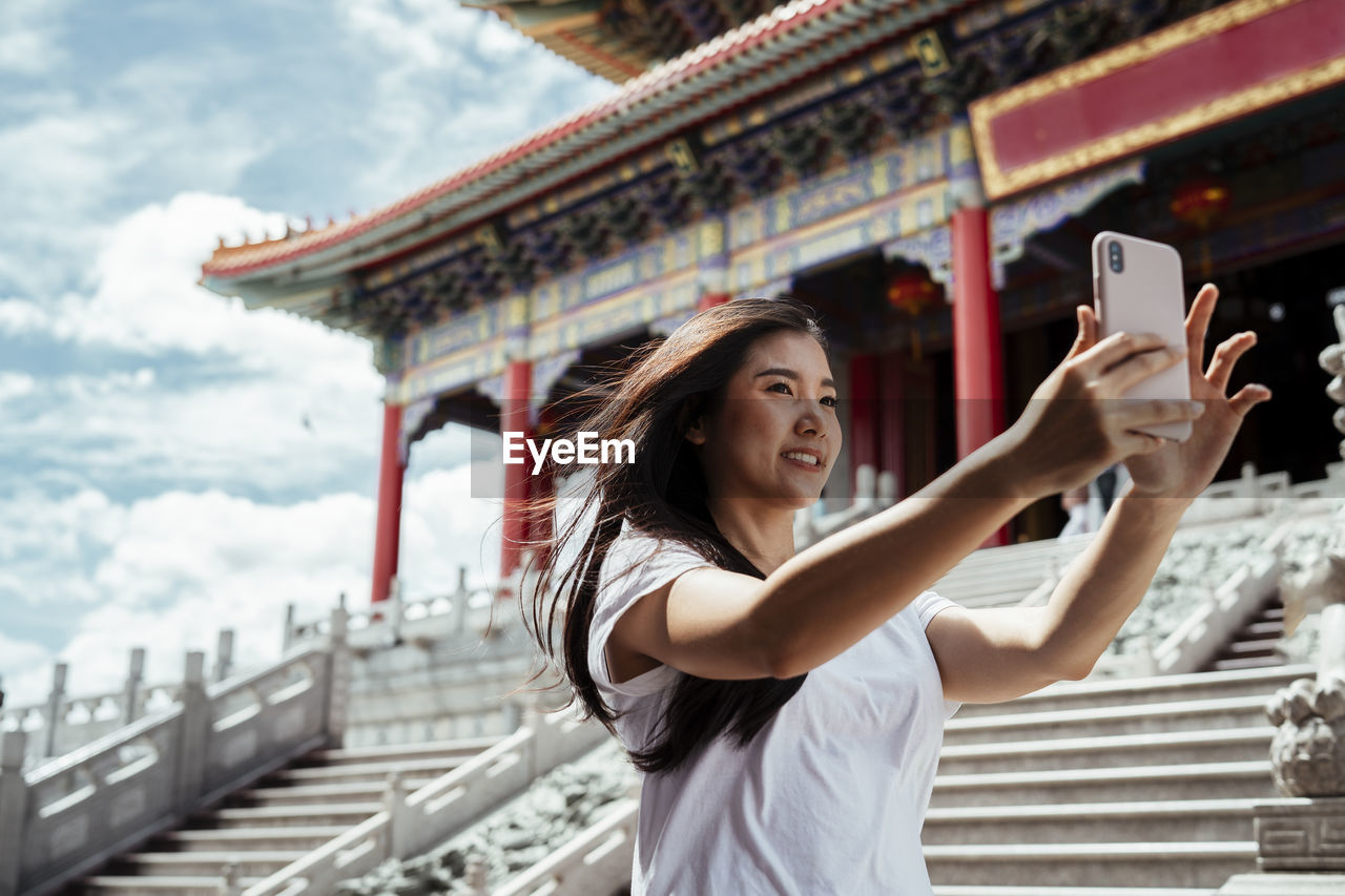 Smiling women vlogging while standing against temple