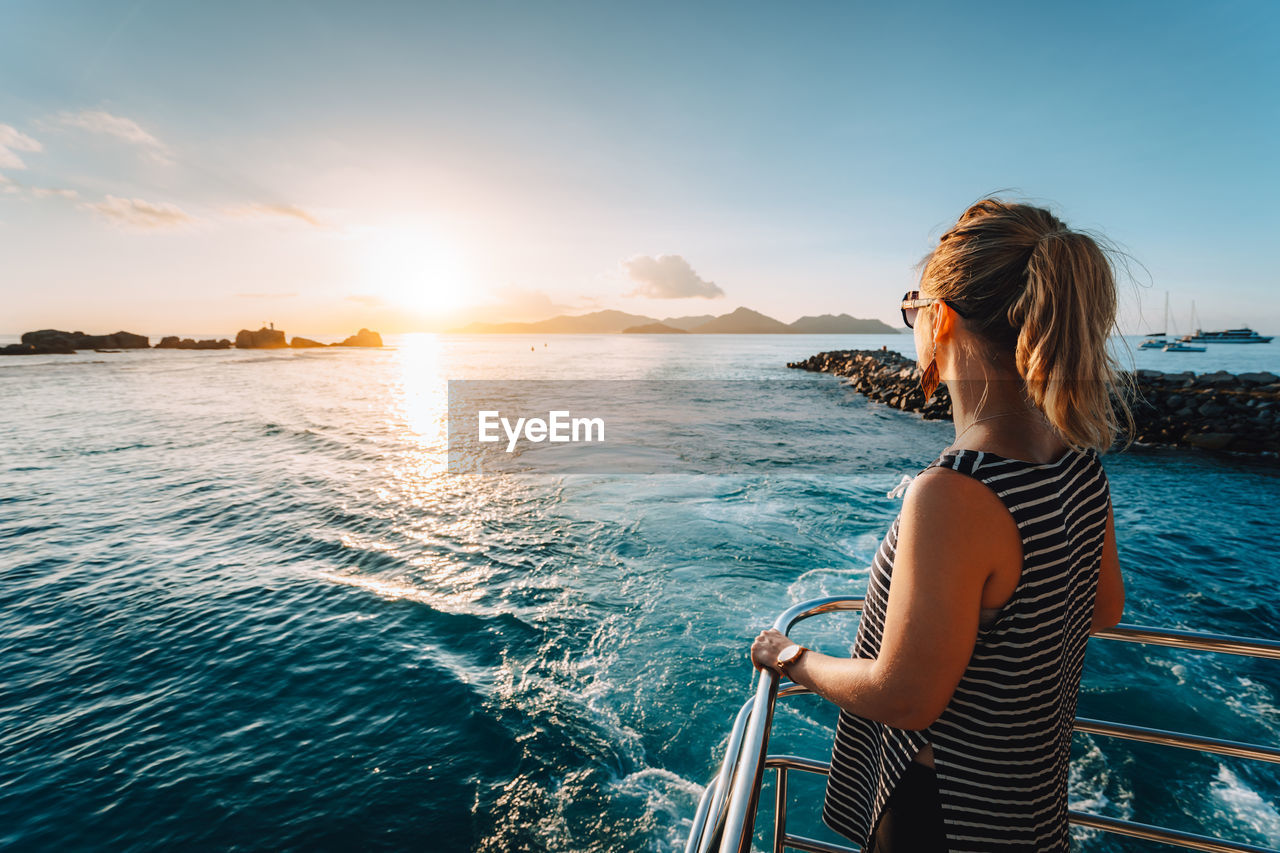 Woman standing by sea against sky during sunset