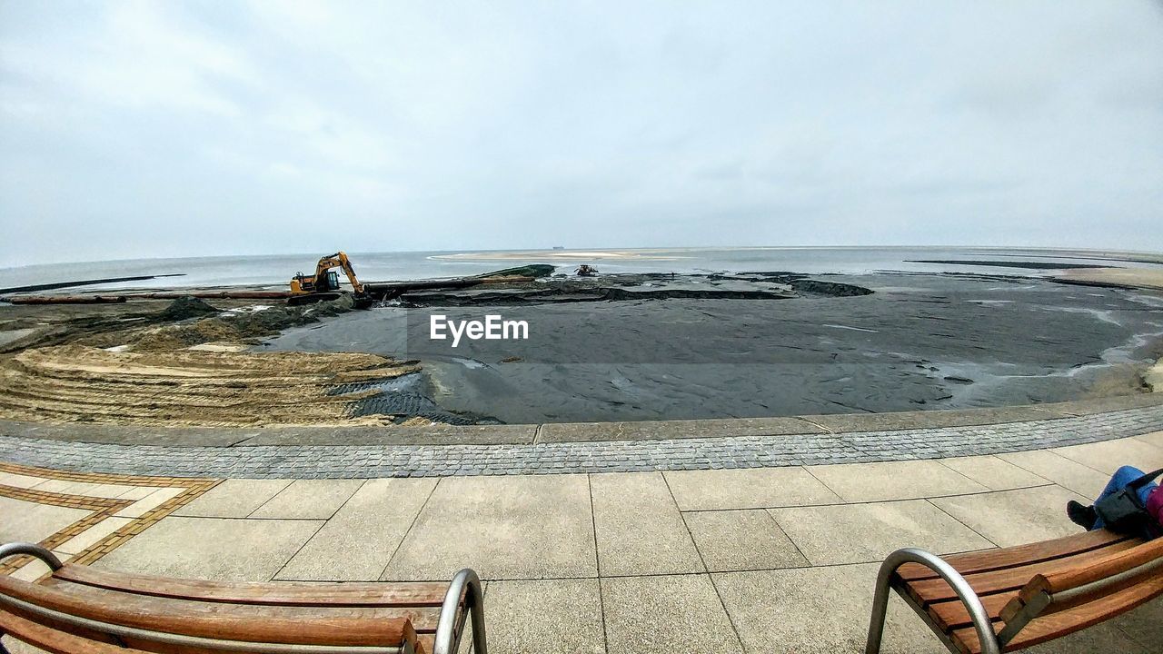 REAR VIEW OF MAN STANDING AT SEA SHORE AGAINST SKY