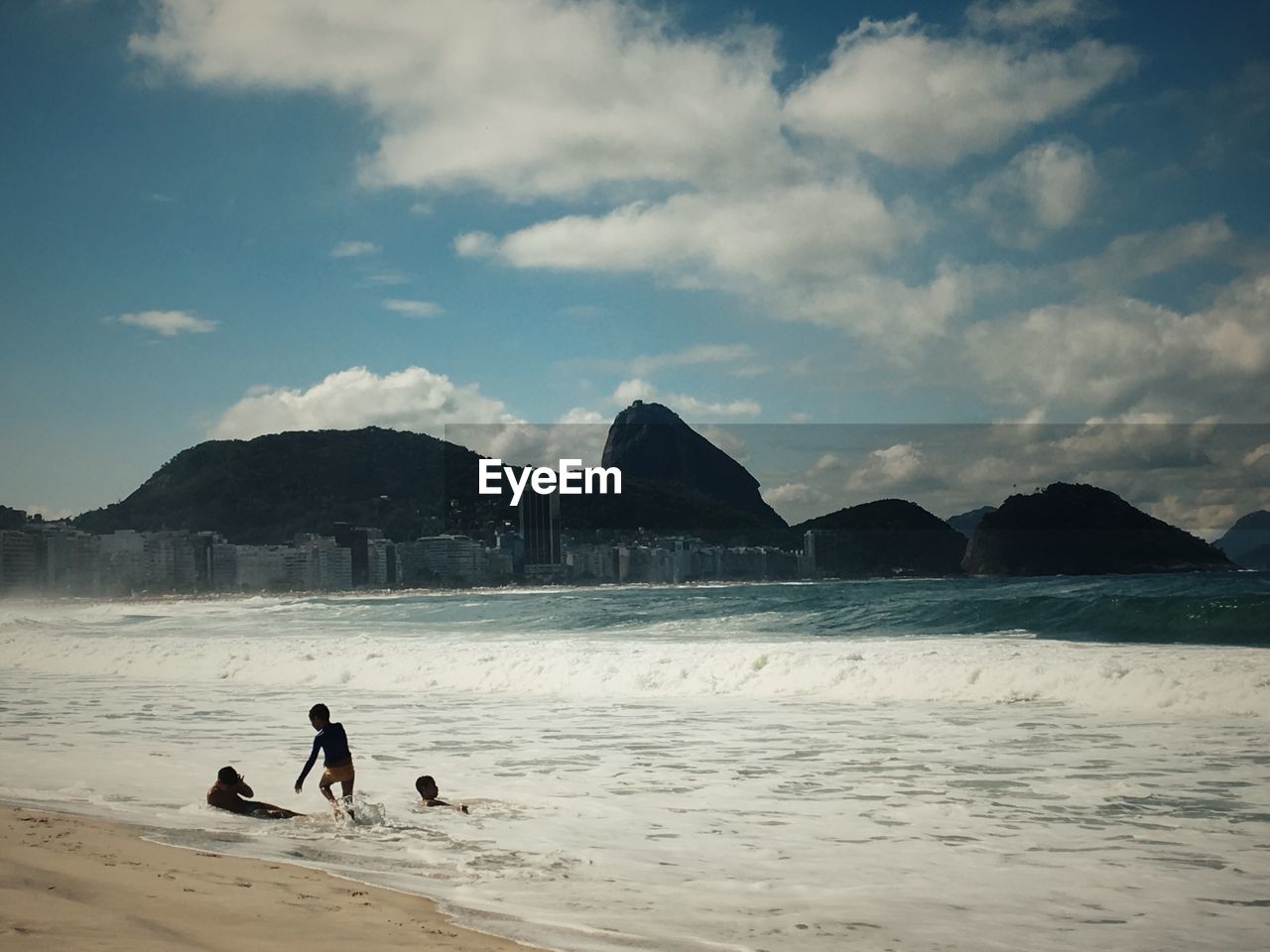 PEOPLE ON BEACH BY MOUNTAIN AGAINST SKY