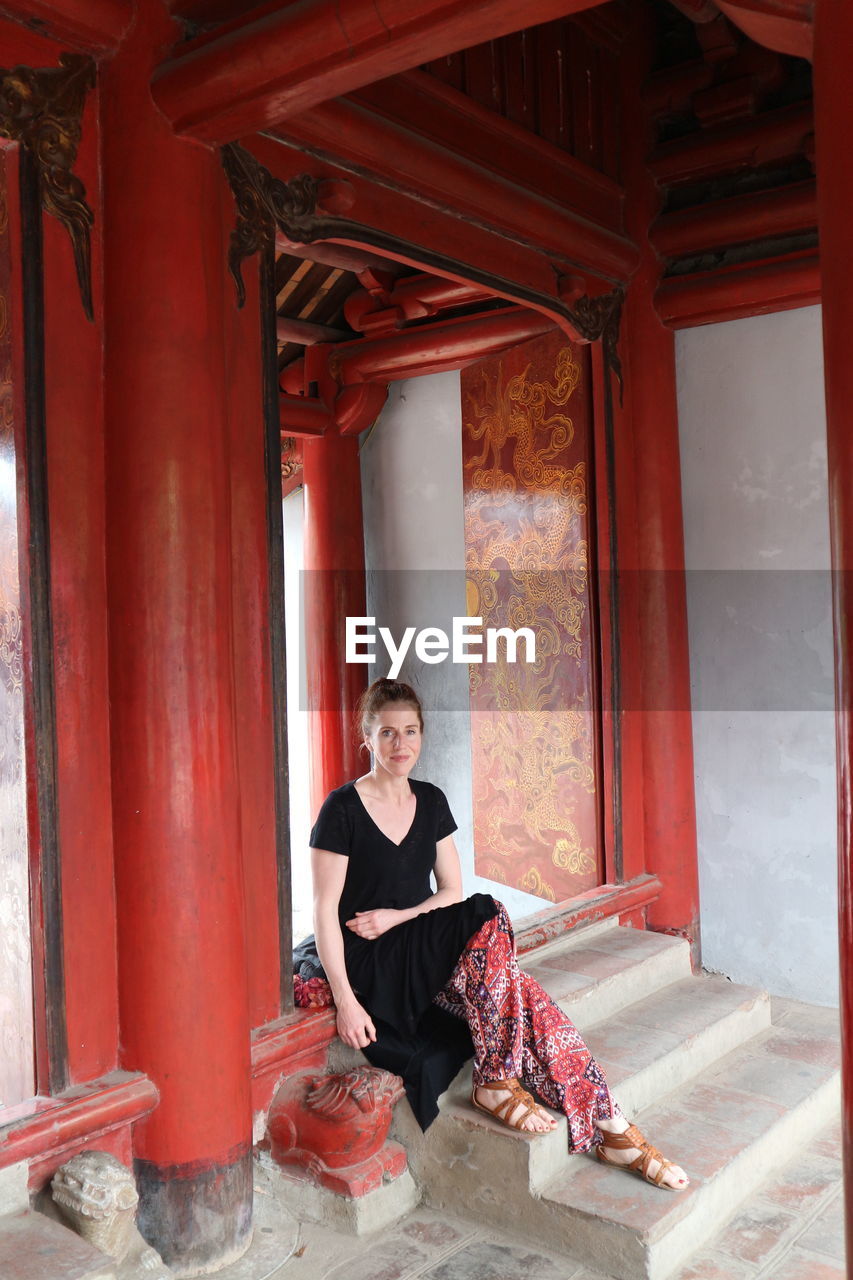 Full length portrait of woman sitting on steps at temple