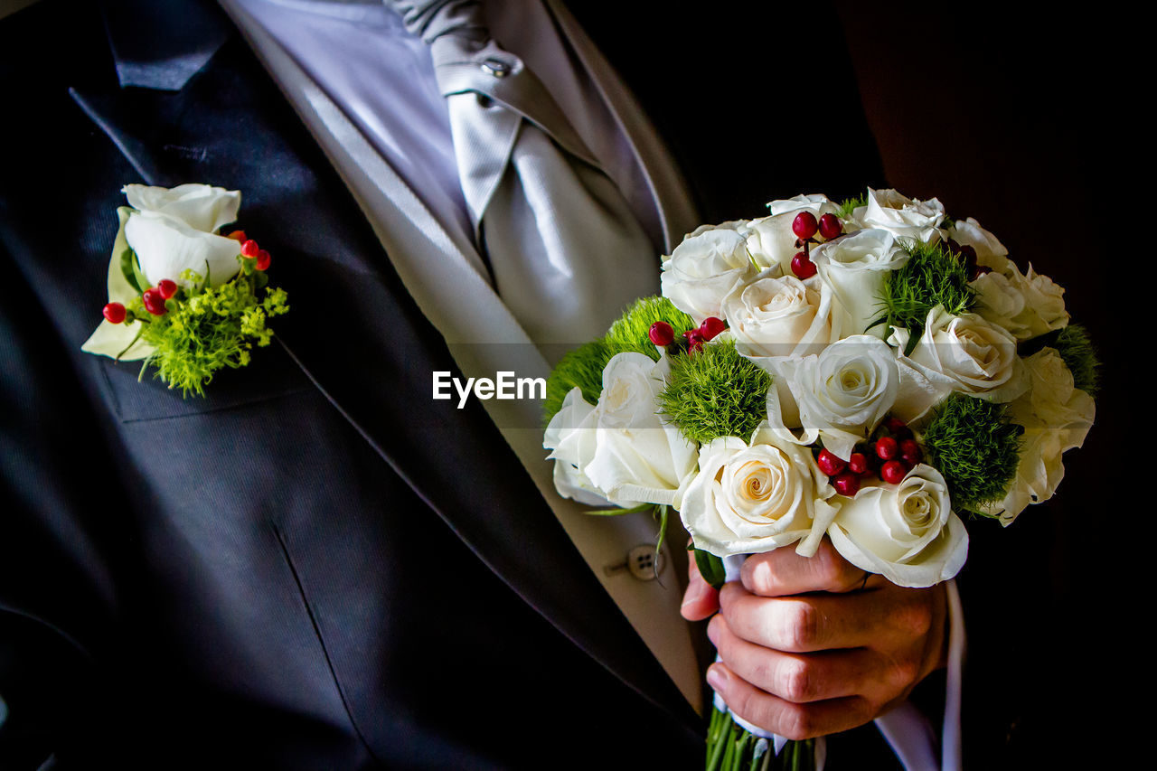 Midsection of groom holding flower bouquet