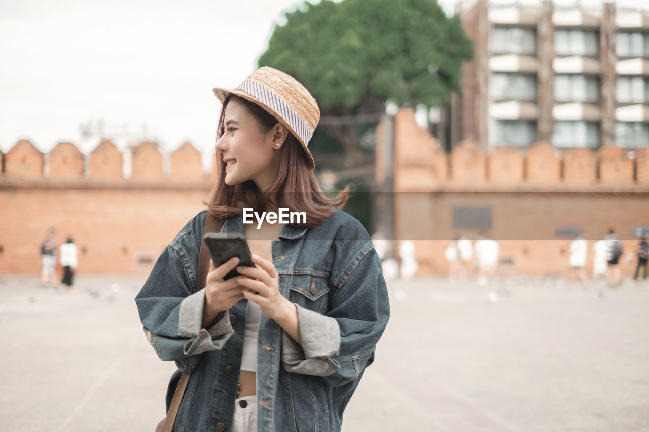 YOUNG WOMAN LOOKING AT CAMERA WHILE STANDING ON CITY