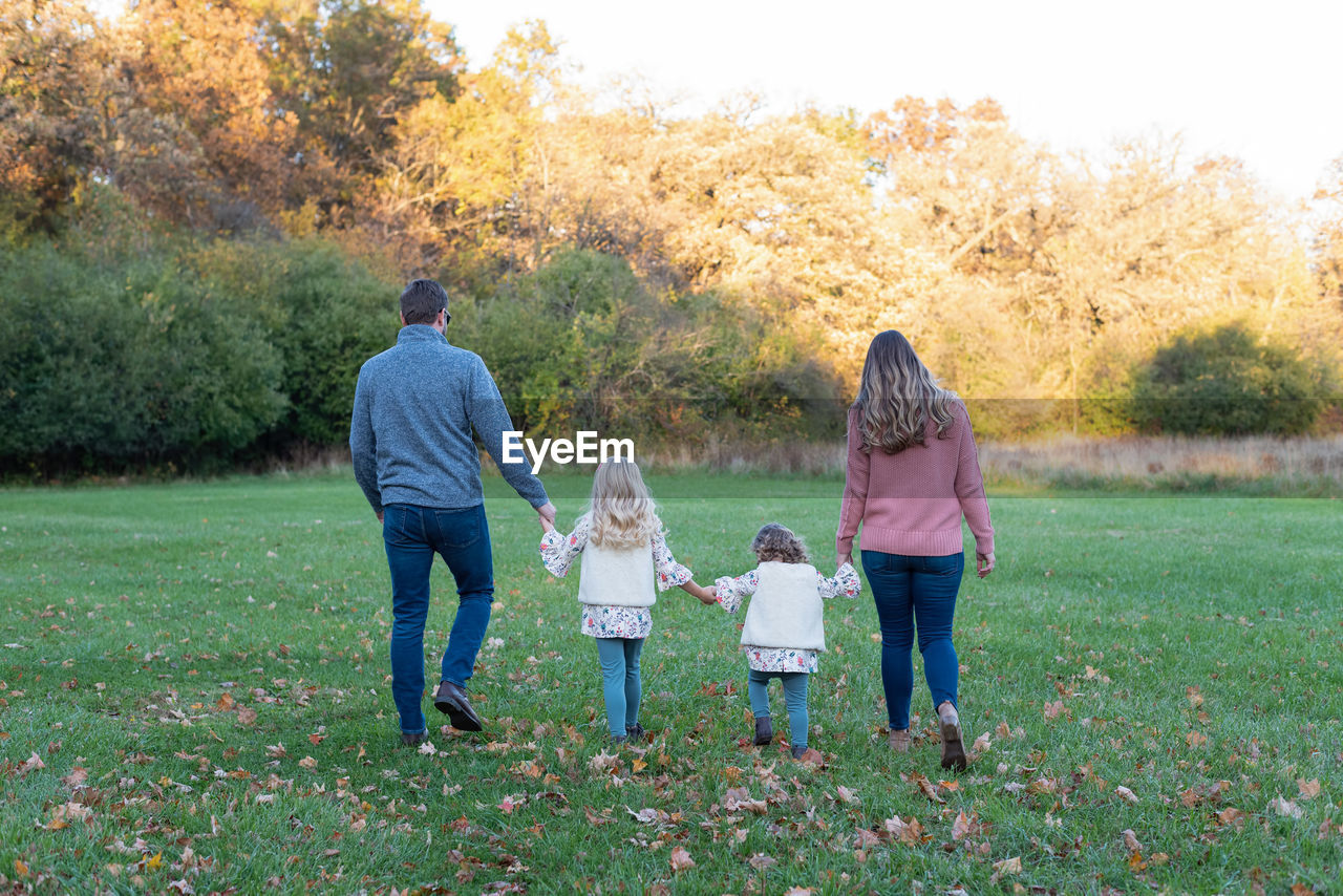 Rear view of friends standing on grass against trees