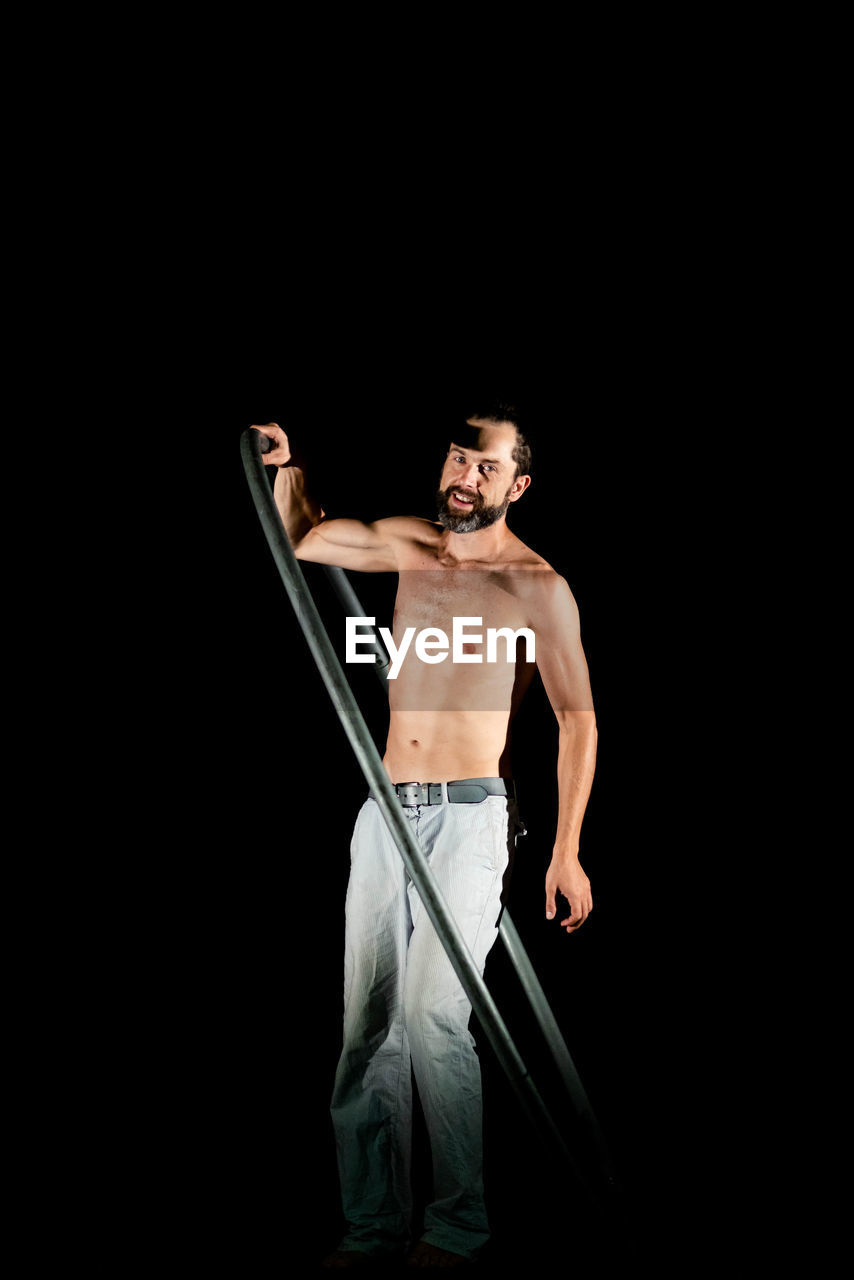 FULL LENGTH OF SHIRTLESS MAN STANDING AGAINST BLACK BACKGROUND