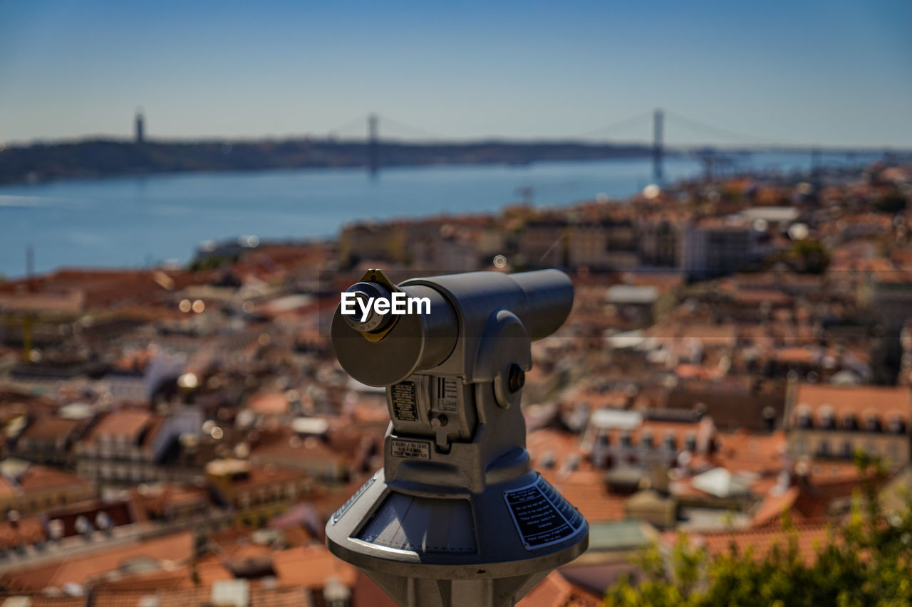 CLOSE-UP OF COIN-OPERATED BINOCULARS CITYSCAPE AGAINST SEA