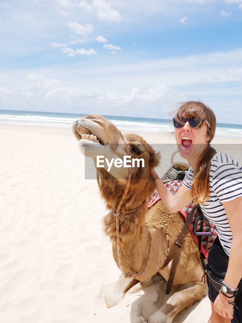 Woman with camel standing at beach against sky