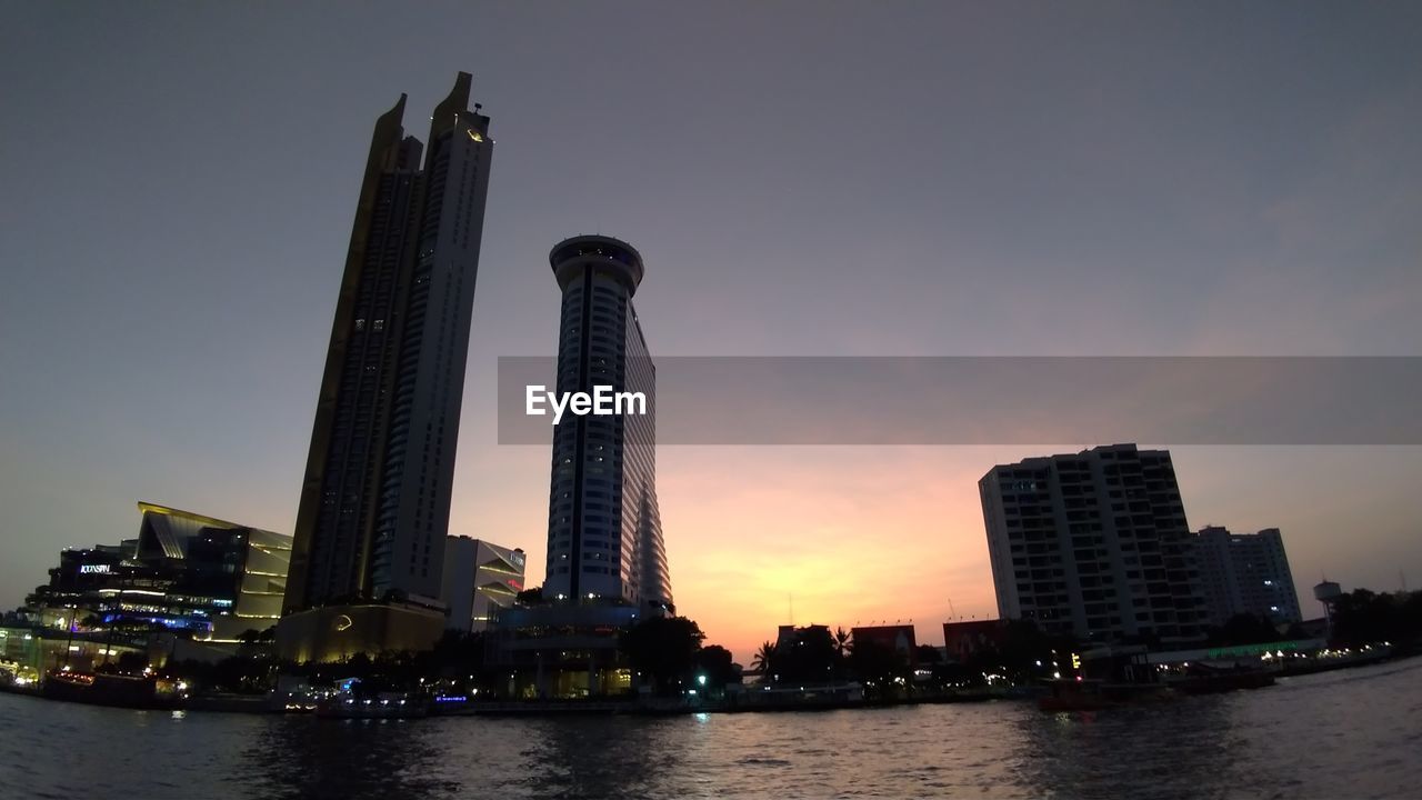 River in city against sky during sunset