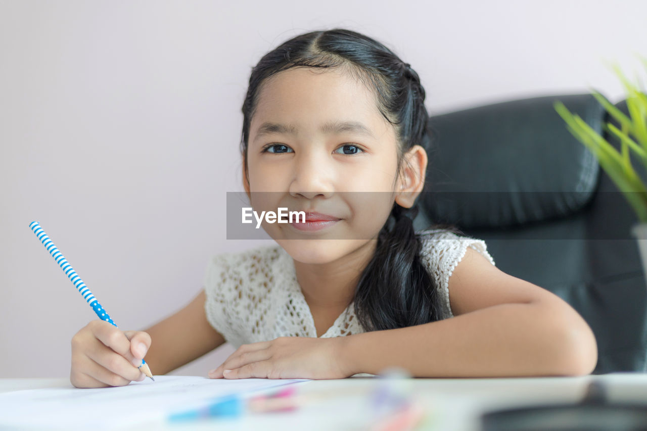 Portrait of cute girl writing in paper against white background