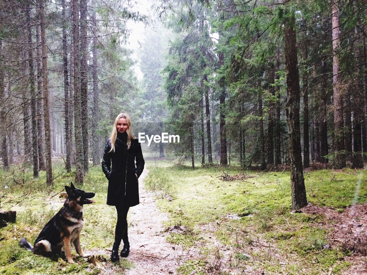 Portrait of woman with dog standing on field at forest