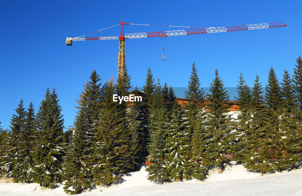 Trees and crane on snowy field against clear sky